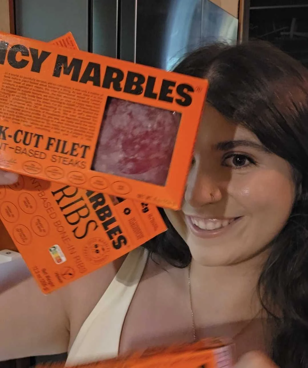 ToniMarie smiling while holding bright orange Juicy Marbles plant-based steak and ribs boxes